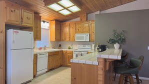 A kitchen with wooden cabinets, a white refrigerator, a microwave, a stove, and a small island with bar stools. - Mountain Modern Pine Mountain Lake Retreat / Near Yosemite + Lake Access (Groveland)
