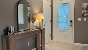 A hallway with a wooden ceiling, a console table with a mirror, a lamp, and a door with a stained glass window. - Mountain Modern Pine Mountain Lake Retreat / Near Yosemite + Lake Access (Groveland)