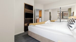 Ein modernes Hotelzimmer mit einem großen Bett, einem Kleiderschrank, einem Fernseher und einer Schiebetür, die auf einen Balkon führt.