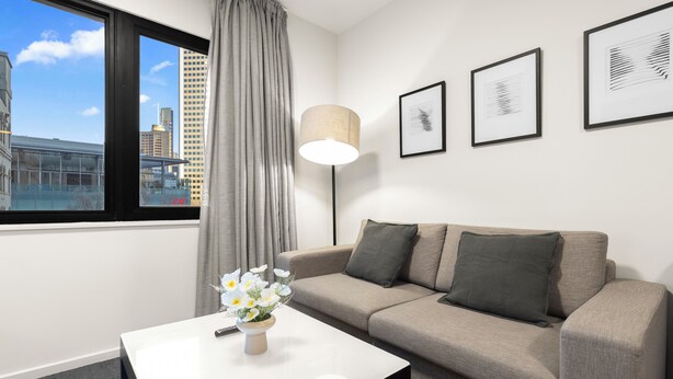Ein modernes Hotelzimmer mit großem Fenster, einer Couch, einem Couchtisch mit Blumenvase und gerahmten Kunstwerken an der Wand.