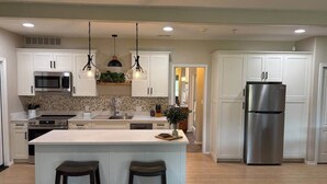 Una cocina moderna con armarios blancos, un refrigerador de acero inoxidable y una isla central con taburetes.