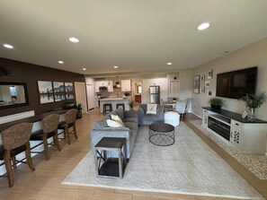 A spacious living room with a sofa, chairs, a coffee table, a TV, and a kitchen in the background. - 1, 2 or 3 rooms|Couples Retreat|Riverfront|Firepit (Spokane County)