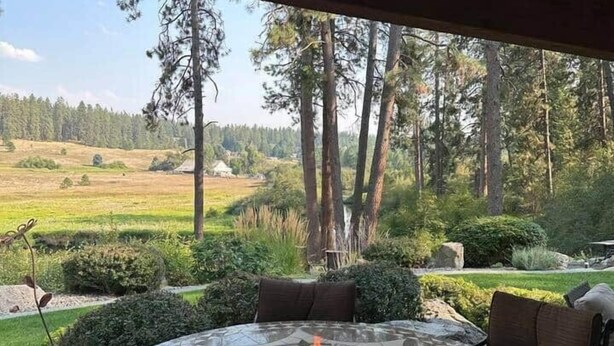 Un espacio de estar al aire libre circular con un brasero, rodeado por una mesa con mosaicos, con vistas a un paisaje boscoso.