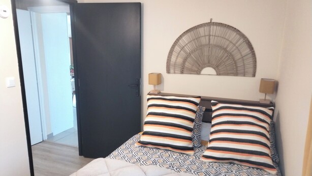 A bedroom with a bed, two bedside lamps, a patterned rug, and a door leading to another room. - Close to Lac de Grand-Lieu, terrace, private parking (La Chevrolière)