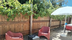 A wooden fence, two red plastic chairs, a small table, and a white umbrella in a shaded outdoor area. - Close to Lac de Grand-Lieu, terrace, private parking (La Chevrolière)