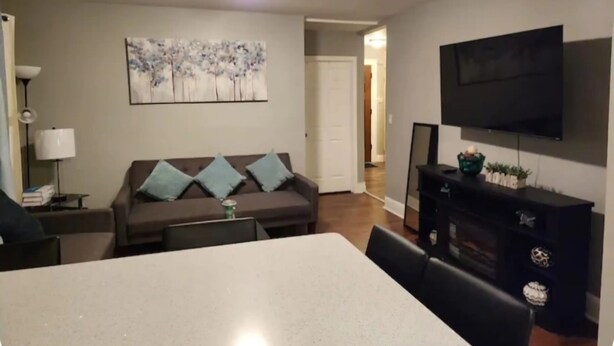 Ein Wohnzimmer mit einer Couch, einem Esstisch, einem an der Wand montierten Fernseher und einem Gemälde über der Couch.