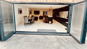 Ett öppet vardags- och matrum med en tegelvägg, en platt-TV, ett kök med en bänkskiva i marmor och en skjutdörr i glas som leder ut till ett utomhusområde.