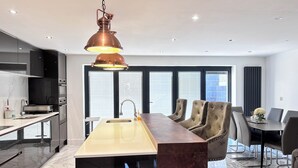 Ett modernt kök med en central köksö, rostfria vitvaror och en hängande lampa i koppar.