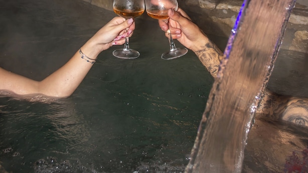 Twee personen proosten met wijnglazen in een jacuzzi met uitzicht op een stadsbeeld 's nachts.