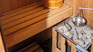 Een houten sauna met een bank, een houten wasbak en een metalen bak met stenen.