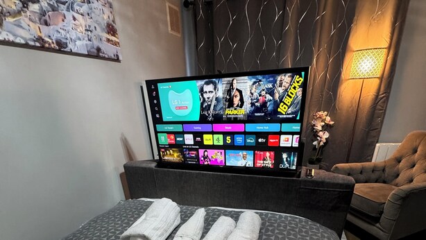 Een hotelkamer met een bed, een televisie waarop een streamingdienst draait, een stoel en een schilderij aan de muur.