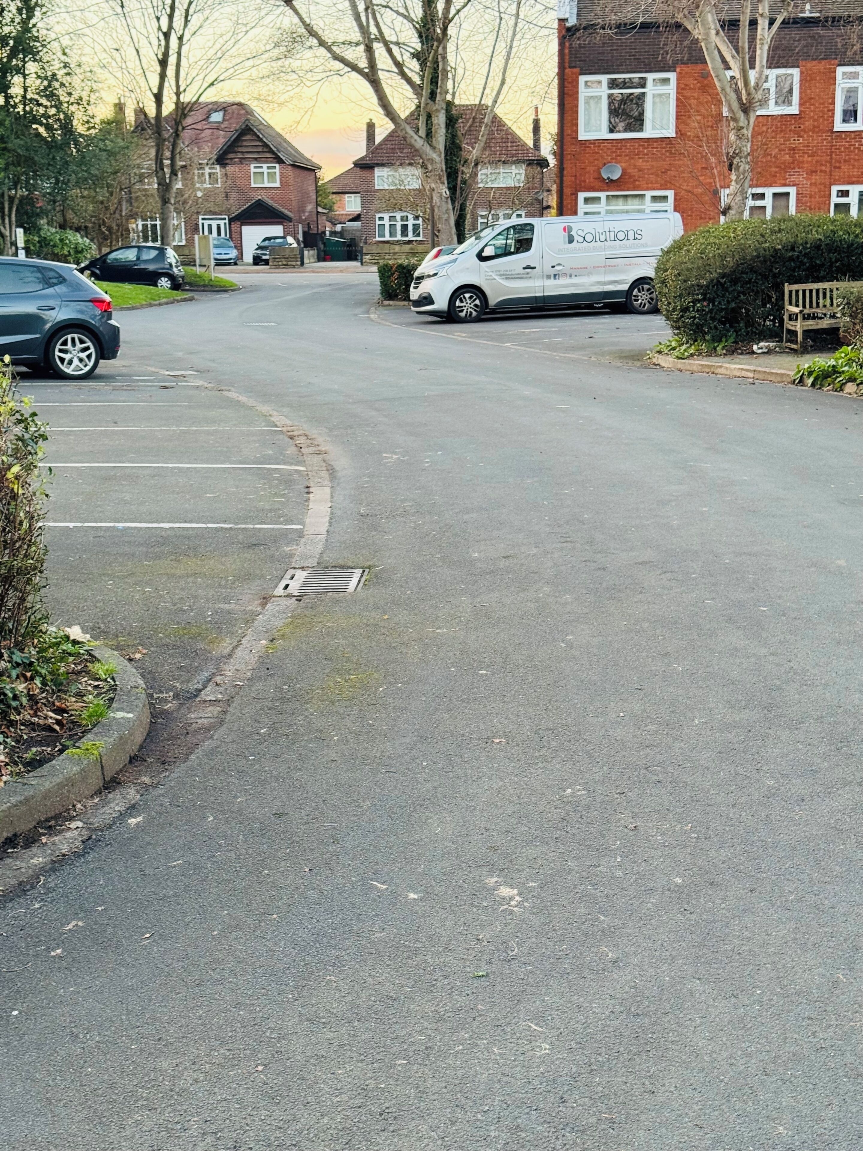 A residential street with parked cars and houses.
