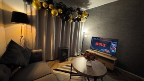 Een woonkamer met een bank, een salontafel, een televisie waarop Netflix wordt afgespeeld, en een decoratieve ballonversiering.