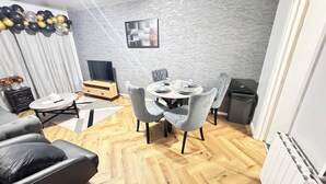 Een moderne woonkamer met een ronde eettafel, grijs gestoffeerde stoelen, een grijze bank, een houten kast en een wand met een grijze structuur.