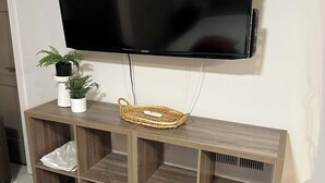 A wooden TV stand with a flat-screen TV mounted above it, a wicker basket, and two potted plants. - Private Guest Suite in Historic Home (Sioux Falls)