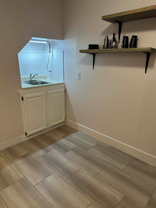 A kitchen with a window, white cabinets, a wooden floor, and a black shelf with kitchen items. - Private Guest Suite in Historic Home (Sioux Falls)