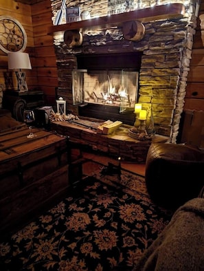 Ein gemütliches Zimmer mit Kamin aus Stein, Holzmöbeln und einem gemusterten Teppich.