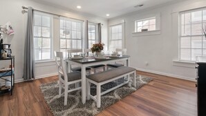 A modern dining area with a white table, grey upholstered chairs, and a bench. - Mara Retreat : Unit A: Fire Pit-Grill-Groups-Patio-Games-Ping Pong Table (Birmingham)