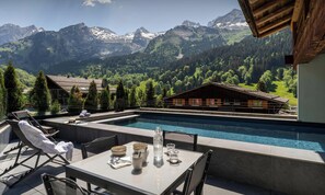Zona de piscina con mesa lista para comer, sillas de descanso y vistas a montañas.