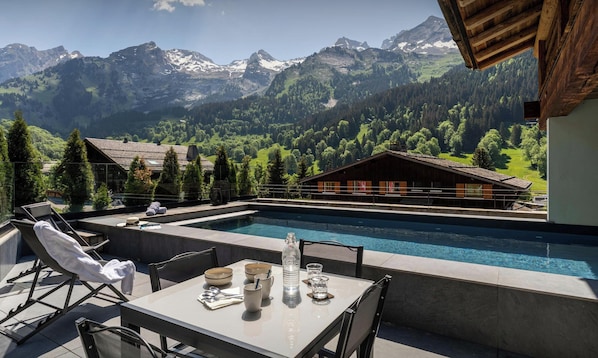A poolside area with a table set for dining, lounge chairs, and a view of mountains. - Chalet Anthocyane - Pamper yourself with spa facilities - OVO Network (La Clusaz)