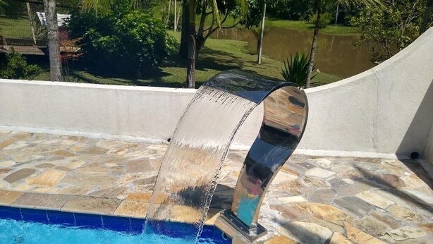 Une piscine dotée d’une terrasse en pierre et d’un élément décoratif aquatique aux formes arrondies.