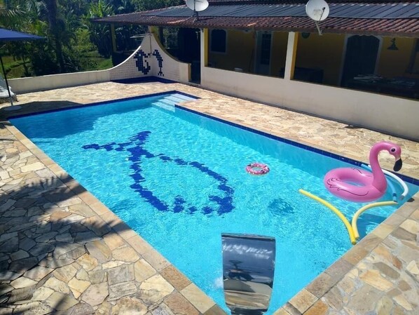 A swimming pool with a stone border, a pink flamingo float, and a heart-shaped design in the water.