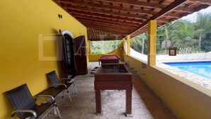 Un espace extérieur abrité comprenant une table de baby-foot, des sièges et une vue sur la piscine.