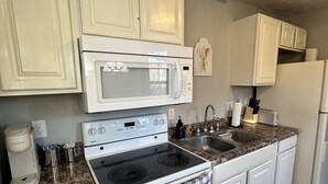 A kitchen with white cabinets, a microwave, stove, sink, and a refrigerator. - Red Brush Cottage Property (Elkton)