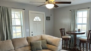 A living room with a sectional sofa, a ceiling fan, a dining table with chairs, and a door with a window. - Red Brush Cottage Property (Elkton)