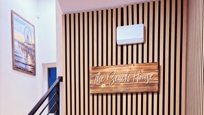 Ein hölzernes Schild mit der Aufschrift "The Beach House" und "EST 2025" an einer Wand mit vertikalen Holzlatten.