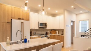 Een moderne keuken met houten kastjes, een centraal eiland met barkrukken, een magnetron en een roestvrijstalen koelkast.