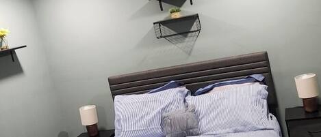 Un lit bien fait, avec une literie à rayures, une tête de lit sombre et deux tables de chevet avec des lampes.