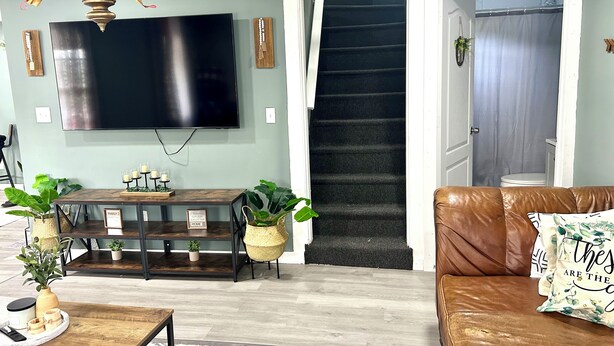 Una sala de estar con un televisor de pantalla plana, una mesa de comedor de madera y un sofá de cuero marrón.