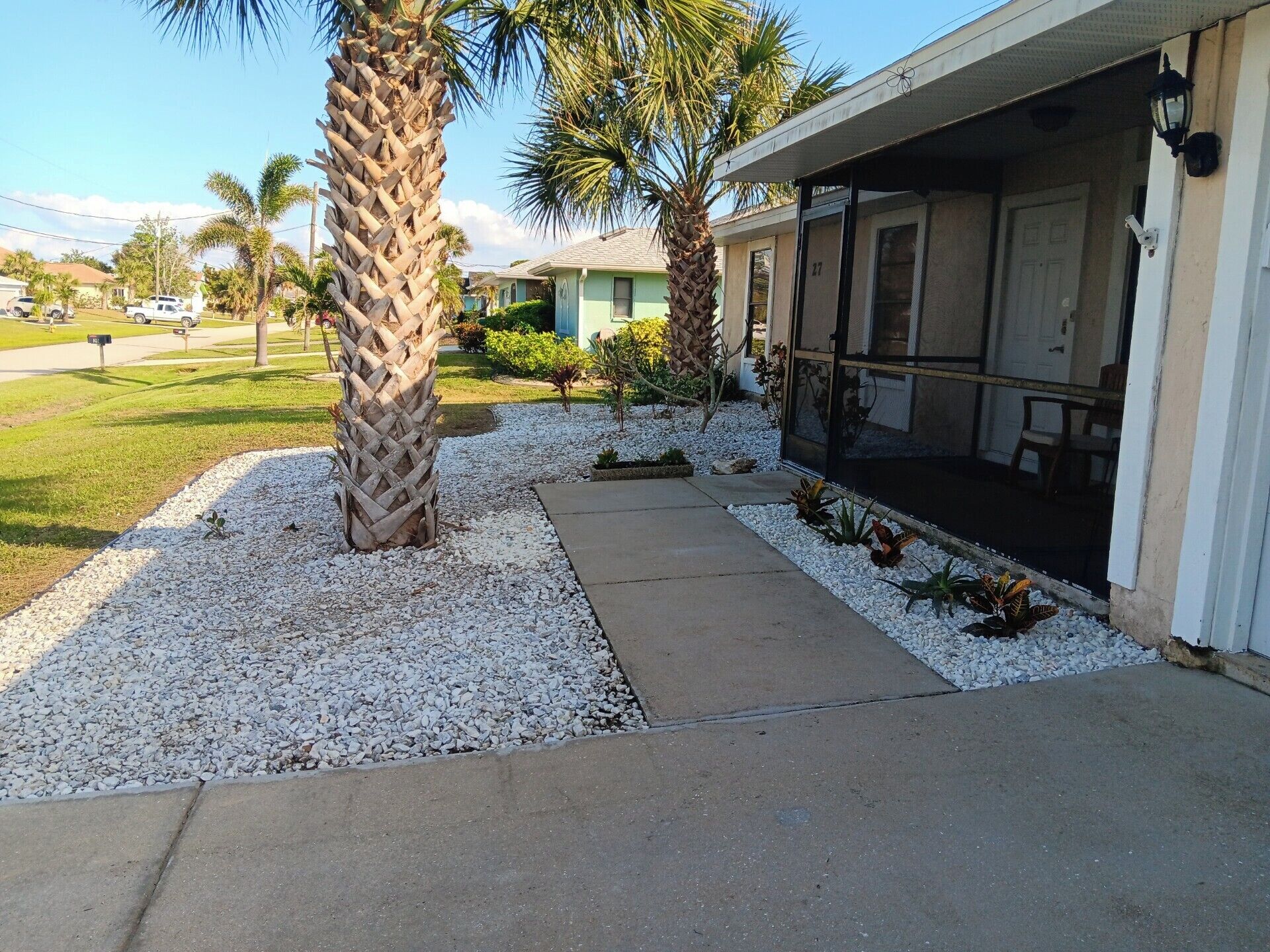 A house with a covered porch, gravel driveway, and palm trees.