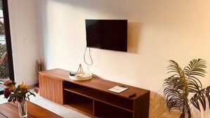 Ett modernt vardagsrum med en platt-TV som är monterad på väggen, en möbel i trä för underhållningsutrustning, ett soffbord och en krukväxt.