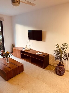 A modern living room with a flat-screen TV mounted on the wall, a wooden entertainment unit, a coffee table, and a potted plant. - Superb New 2 room apartment with great amenities in Playa del Carmen in 38th (Playa del Carmen)