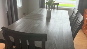 Un área de comedor con una mesa y sillas de madera, un florero con flores y vistas a un paisaje verde a través de una ventana.