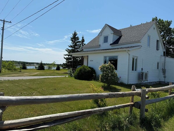 Une maison blanche à deux étages, dotée d’un porche, d’un petit jardin et d’une clôture en bois au premier plan.