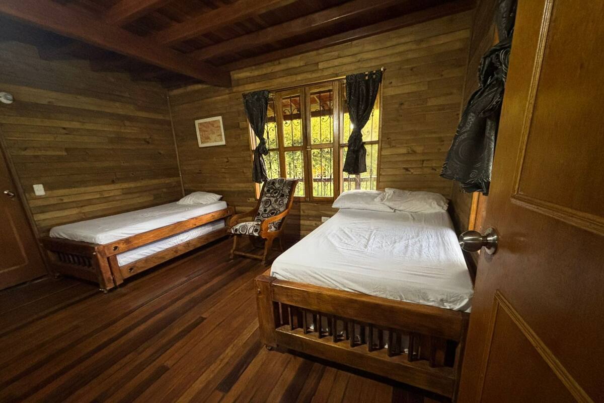 A cabin with two wooden beds, a chair, and a window with curtains.