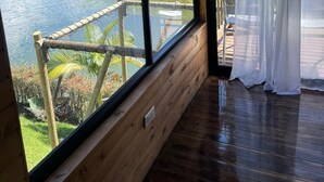 Una stanza con un'ampia finestra vista su uno specchio d'acqua e vegetazione, pareti in legno e un'uscita su un pontile di legno.