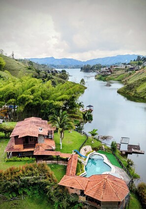 Un resort sul fiume con piscina, edifici in legno e vegetazione rigogliosa.