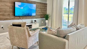 Un soggiorno moderno con una TV a schermo piatto montata su una parete in legno, un tavolino in vetro, un divano color beige e una poltrona.