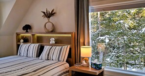 A bedroom with a bed, bedside table, lamp, and a window with a snowy view.