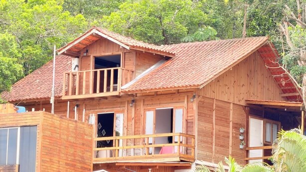 Une cabane en bois dotée d’un balcon, d’une petite dépendance attenante et d’un toit recouvert de tuiles rouges.