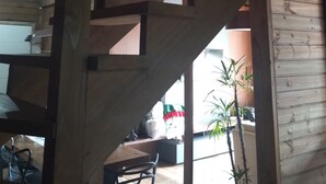 Un escalier en bois offrant une vue sur l’espace intérieur, notamment une table et des chaises, ainsi qu’une fenêtre donnant sur l’extérieur.