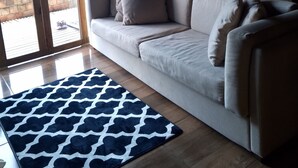 Un salon moderne avec un canapé beige, un tapis à motifs et une grande fenêtre agrémentée de rideaux.