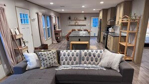 A modern living room with a grey sectional sofa, a wooden coffee table, and a dining area with a kitchen in the background.