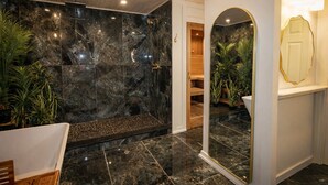 Ein Badezimmer mit Marmorwand, einer Dusche, einem Spiegel und einer Holztür.
