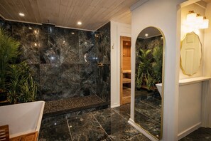 Ein Badezimmer mit Marmorwand, einer Dusche, einem Spiegel und einer Holztür.
