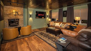 Ein Wohnzimmer mit Kamin aus Stein, einer Ledersofa, einem Couchtisch und einem Fernseher, der 'NETFLIX' zeigt.